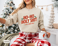 Thumbnail for A woman wearing a beige sweatshirt with a humorous text printed on it, sitting in front of a Christmas tree.