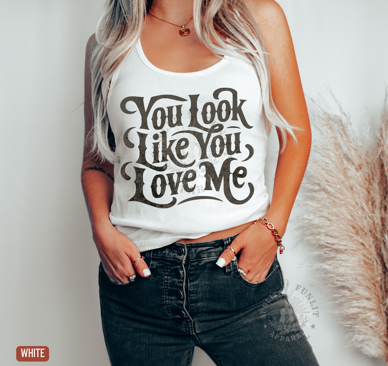 A woman wearing a white tank top with the text "You look like you love me" printed on it.