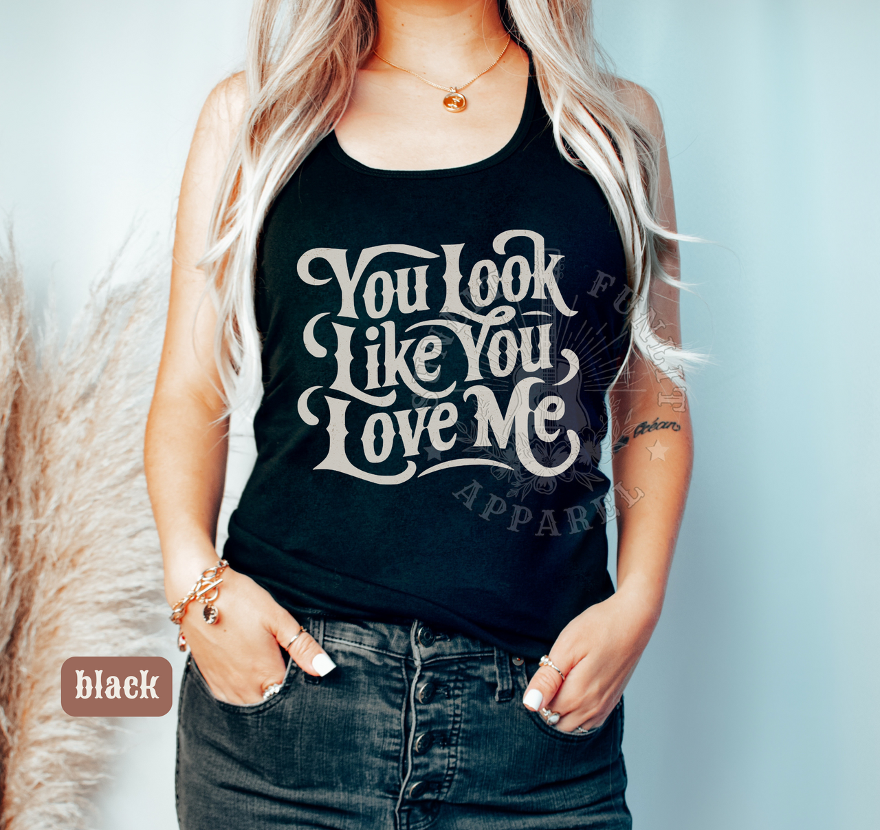 A woman wearing a black tank top with the text "You look like you love me" printed on it.