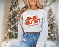 Thumbnail for A woman wearing a grey sweatshirt with a humorous text printed on it, smiling and posing in front of a Christmas tree.