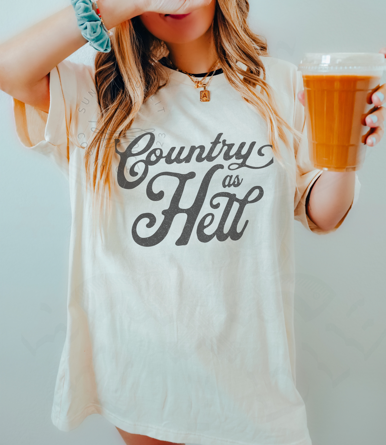 A woman wearing a white t-shirt with the text "Country as Hell" printed on it, holding a drink in her hand.