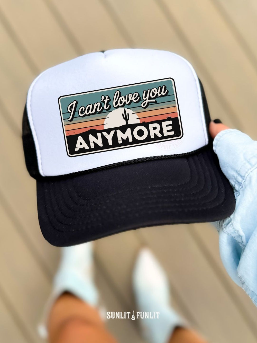 Trucker hat with 'I can't love you anymore' text held by a person wearing white gloves.