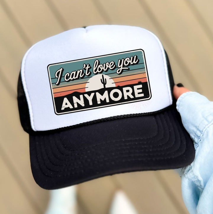 Trucker hat with 'I can't love you anymore' text held by a person wearing white gloves.