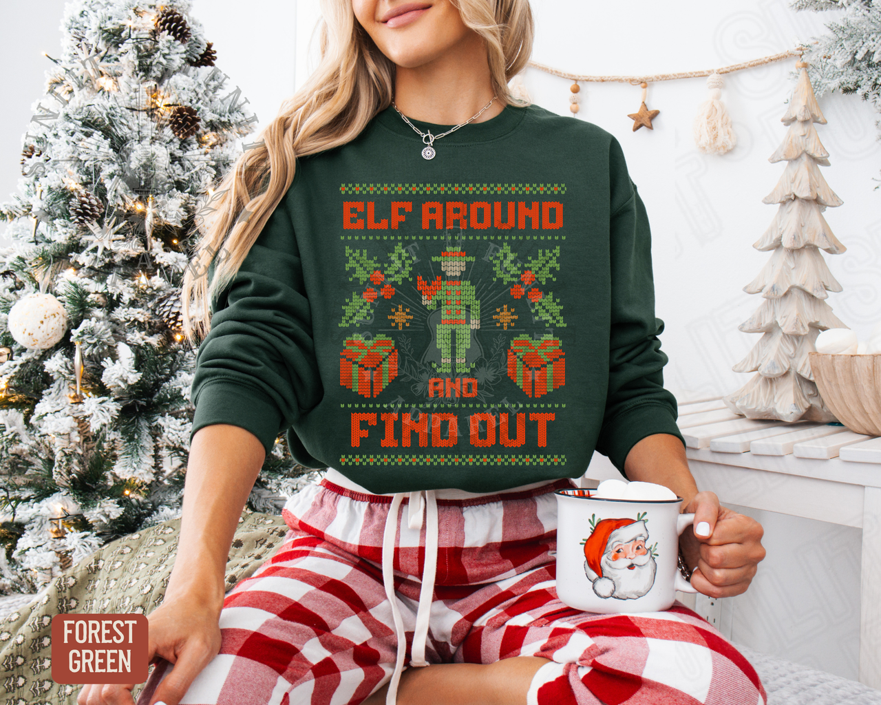 A woman wearing a green sweater with a Christmas-themed design is sitting in front of a Christmas tree, holding a mug with a Santa Claus image.