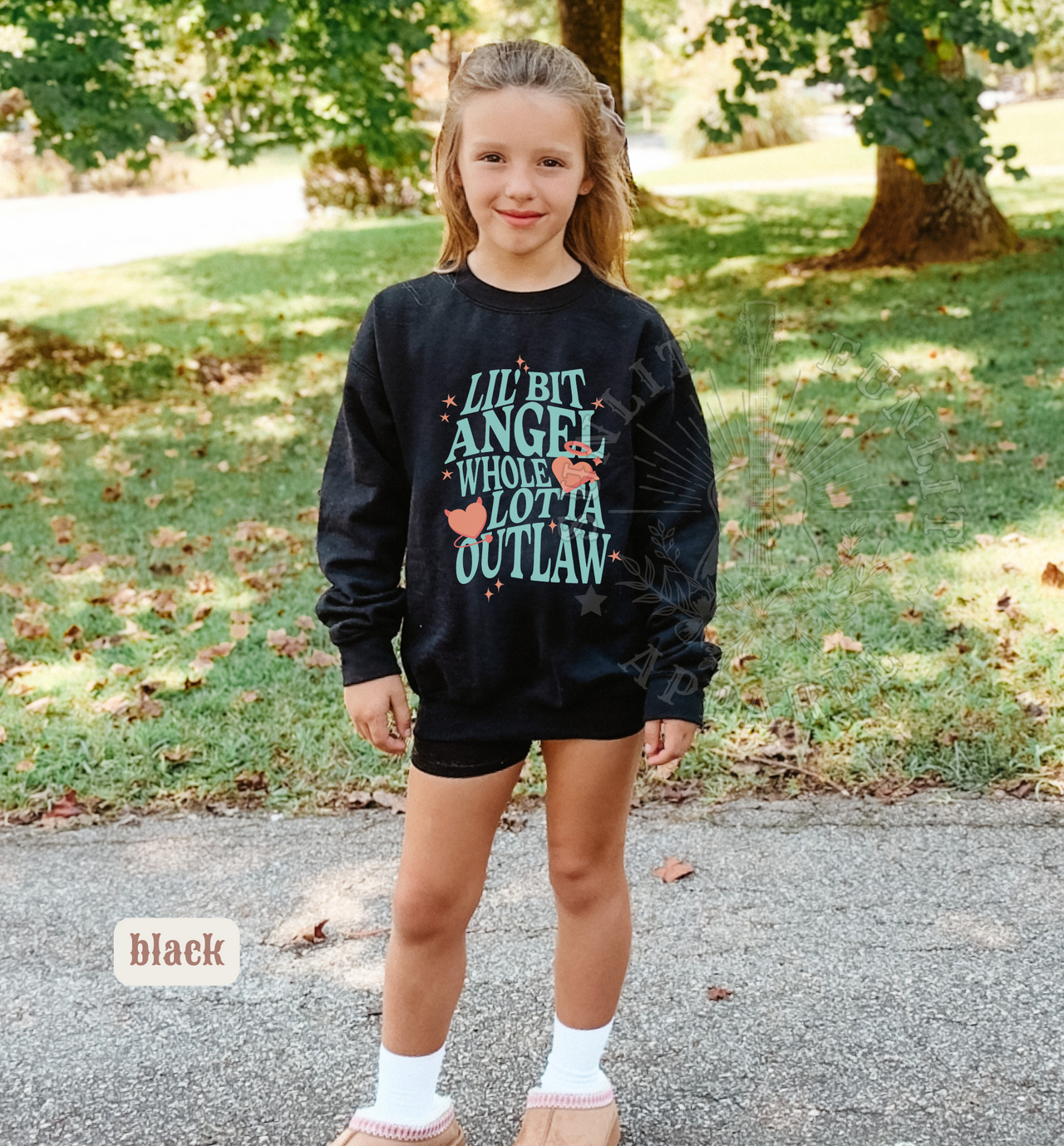 A young girl wearing a black sweatshirt with a graphic design stands on a paved path in a park.