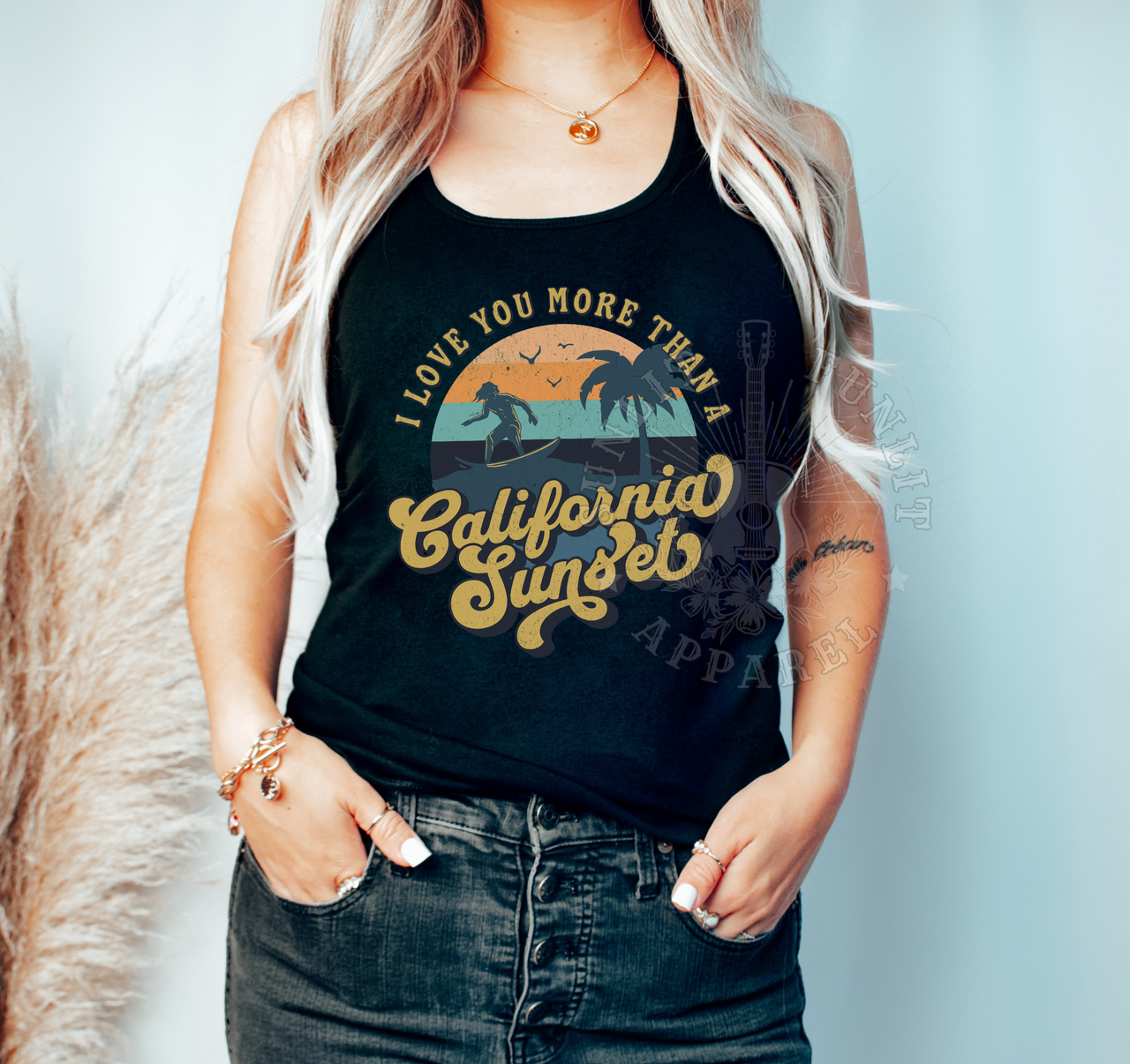 A woman wearing a black tank top with a graphic design that says "I LOVE YOU MORE THAN A CALIFORNIA SUNSET" and jeans.