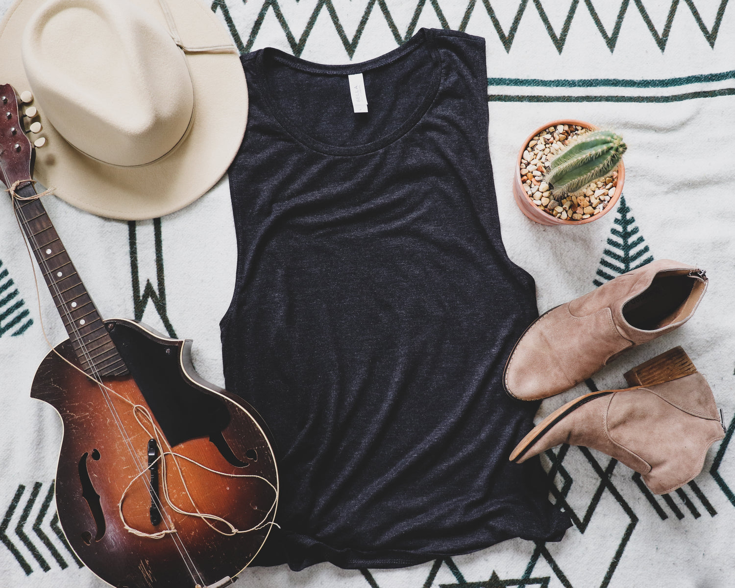Black tank top with a mandolin, cowboy hat, boots, and cactus on a patterned surface