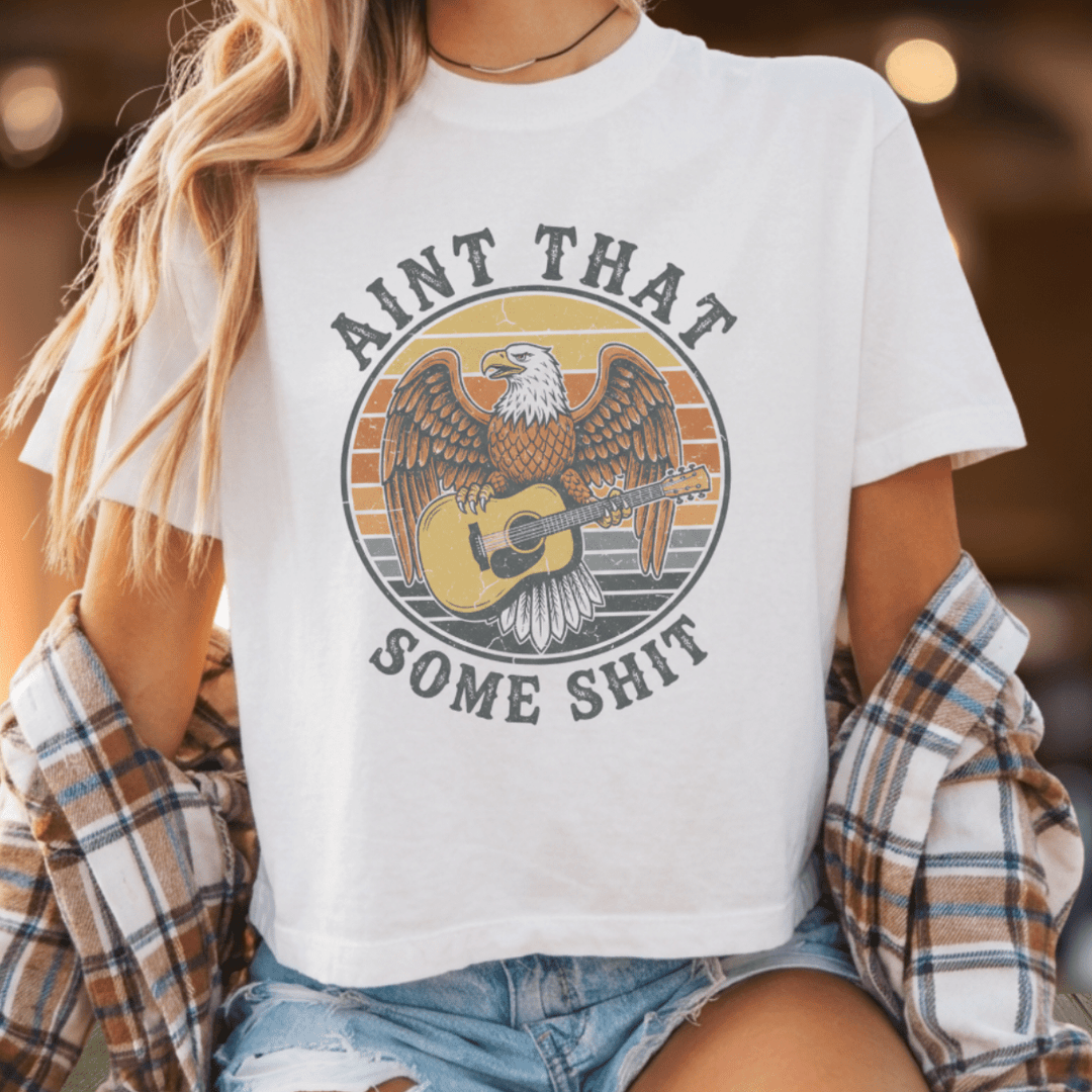 Person wearing a white t-shirt with an eagle graphic and text, sitting outdoors.