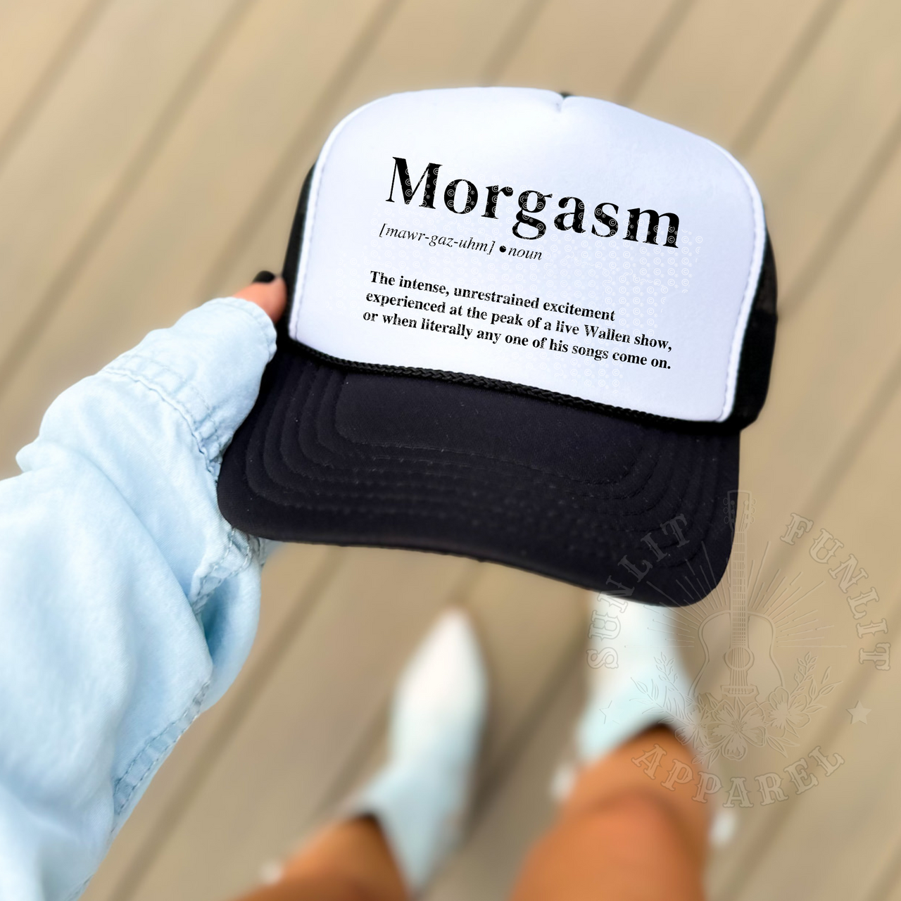 A person is holding a black and white baseball cap with the word "Morgasm" printed on it.