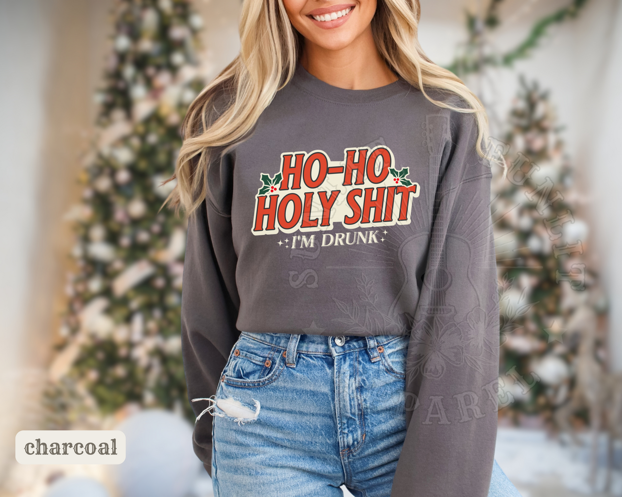 A woman wearing a gray sweatshirt with a humorous text printed on it, smiling and posing in front of a Christmas tree.