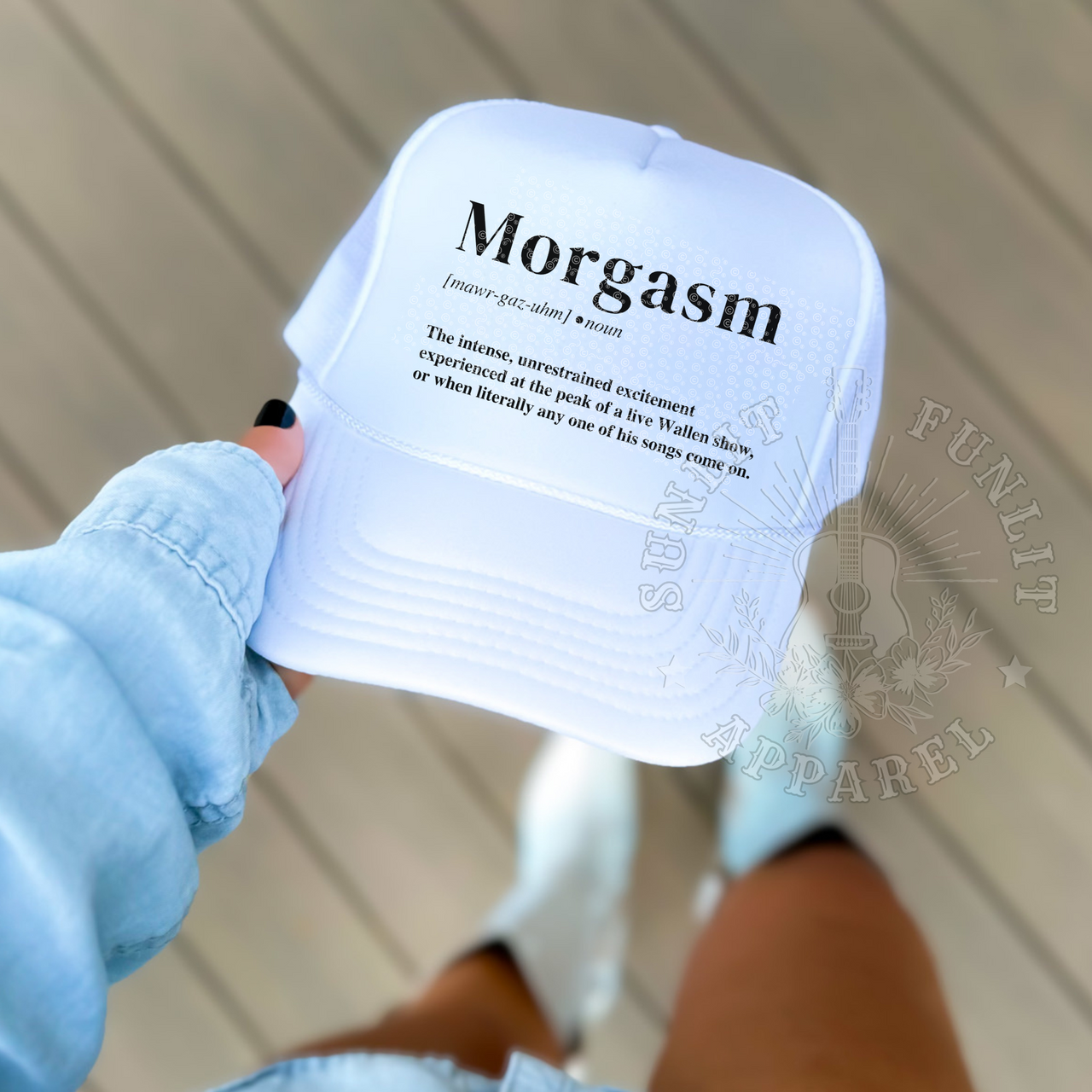A person is holding a white baseball cap with the word "Morgasm" printed on it.