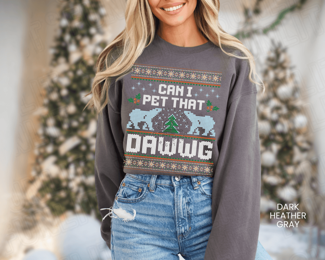 A woman wearing a gray sweatshirt with a Christmas-themed design and text, standing in front of a Christmas tree.