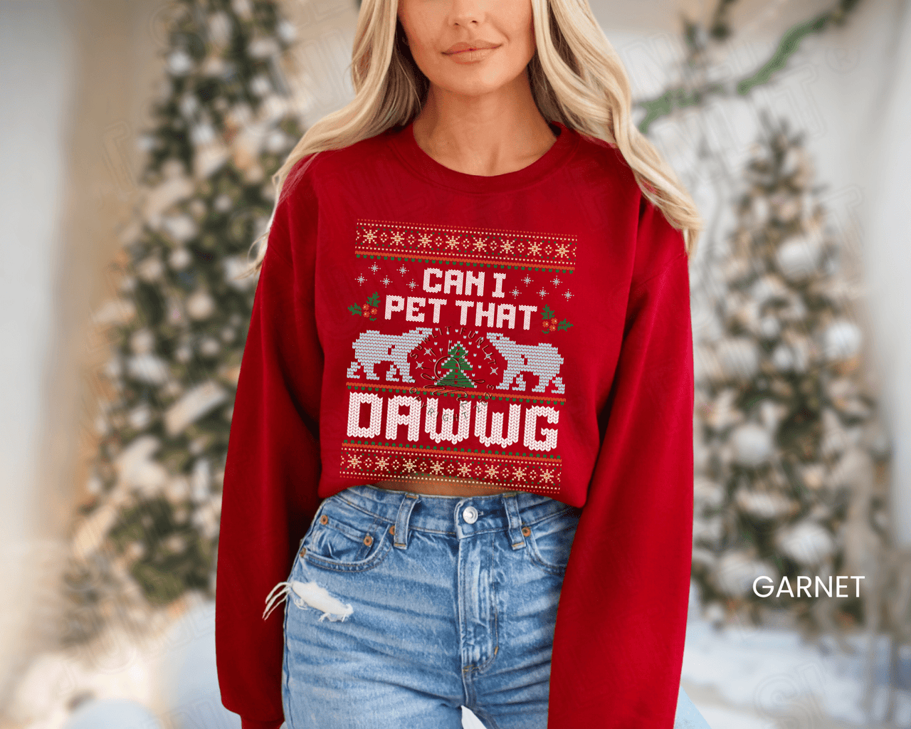 A woman wearing a red sweater with a Christmas-themed design and text, standing in front of a Christmas tree.