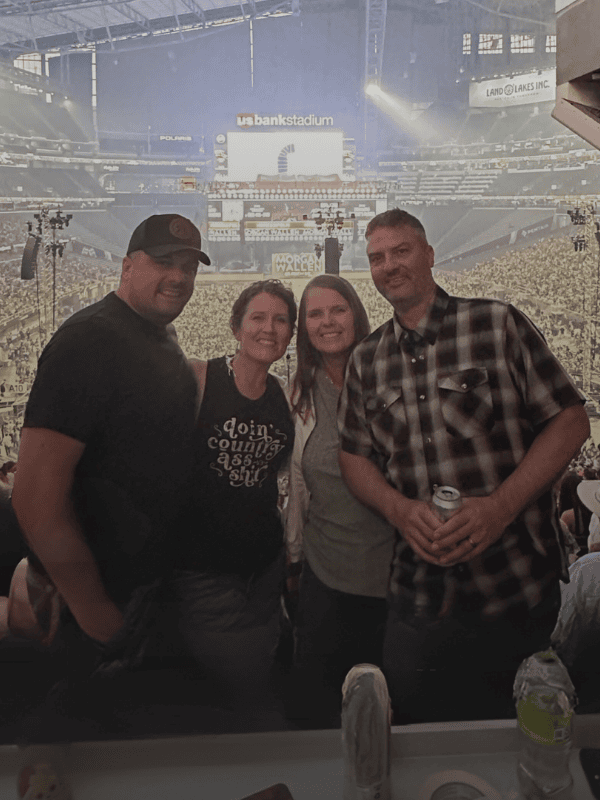 Four people posing for a photo at a sports event in a large stadium.