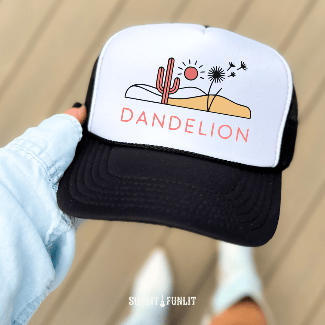Trucker hat with desert graphic and 'Dandelion' text held by a hand against a neutral background