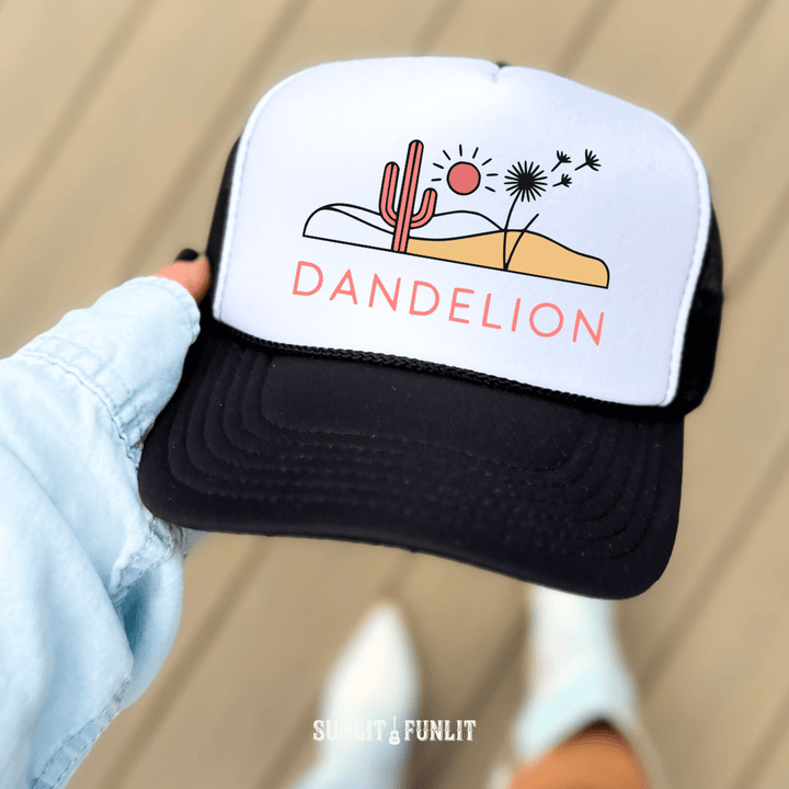 Trucker hat with desert graphic and 'Dandelion' text held by a hand against a neutral background
