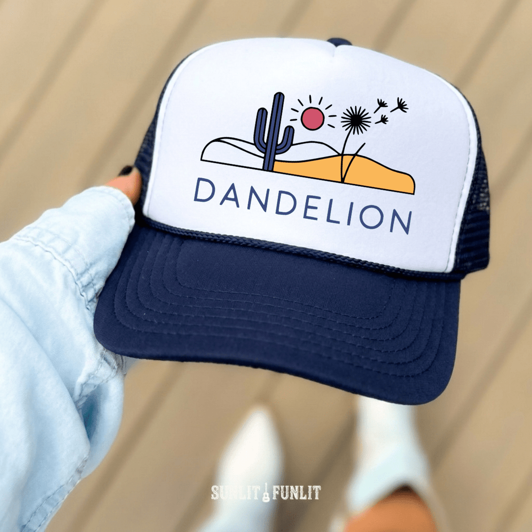 Trucker hat with desert graphic and 'Dandelion' text held by a hand against a neutral background