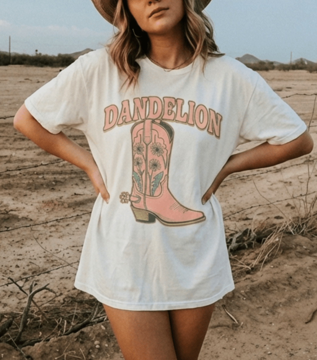 Person wearing a white t-shirt with a pink cowboy boot graphic and 'Dandelion' text in a desert setting.