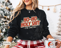 Thumbnail for A woman wearing a black sweatshirt with a humorous Christmas-themed design, holding a mug with a Santa Claus image, and standing in front of a Christmas tree.