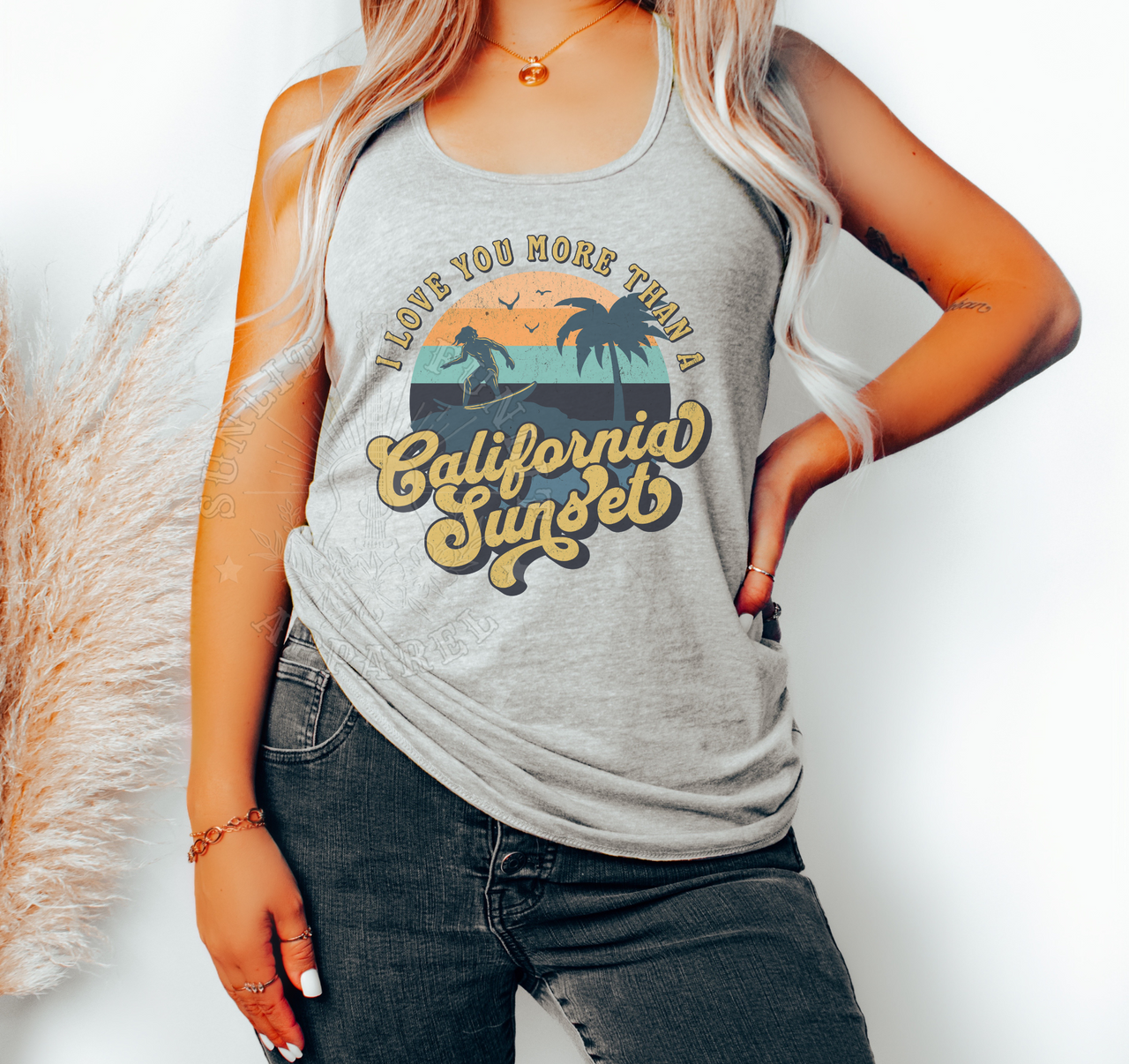 A woman wearing a gray tank top with a graphic design of a sunset and palm trees, along with the text "I LOVE YOU MORE THAN A CALIFORNIA SUNSET".