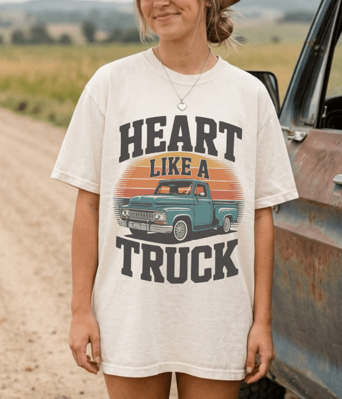 Person wearing a t-shirt with 'Heart Like a Truck' graphic design standing next to an old truck on a dirt road.
