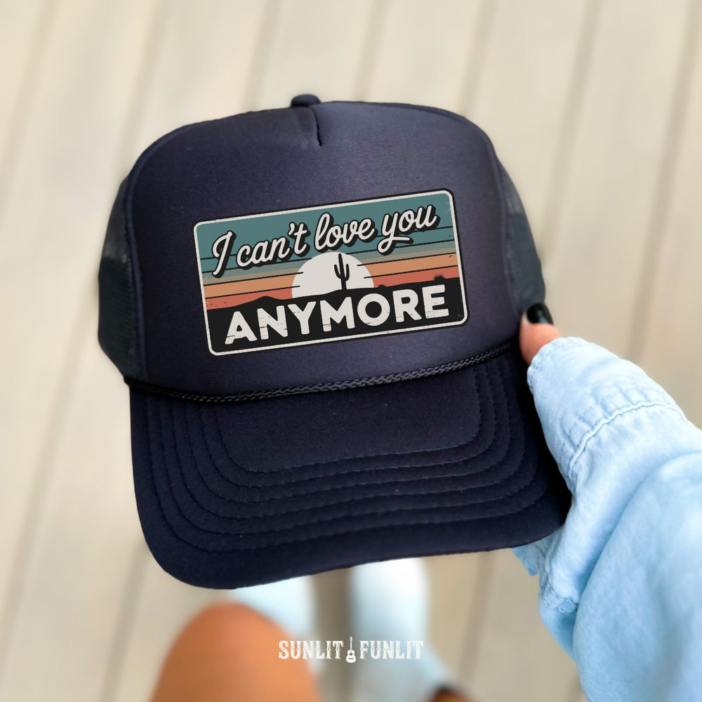Navy blue cap with 'I can't love you anymore' text held by a person wearing a light blue jacket.