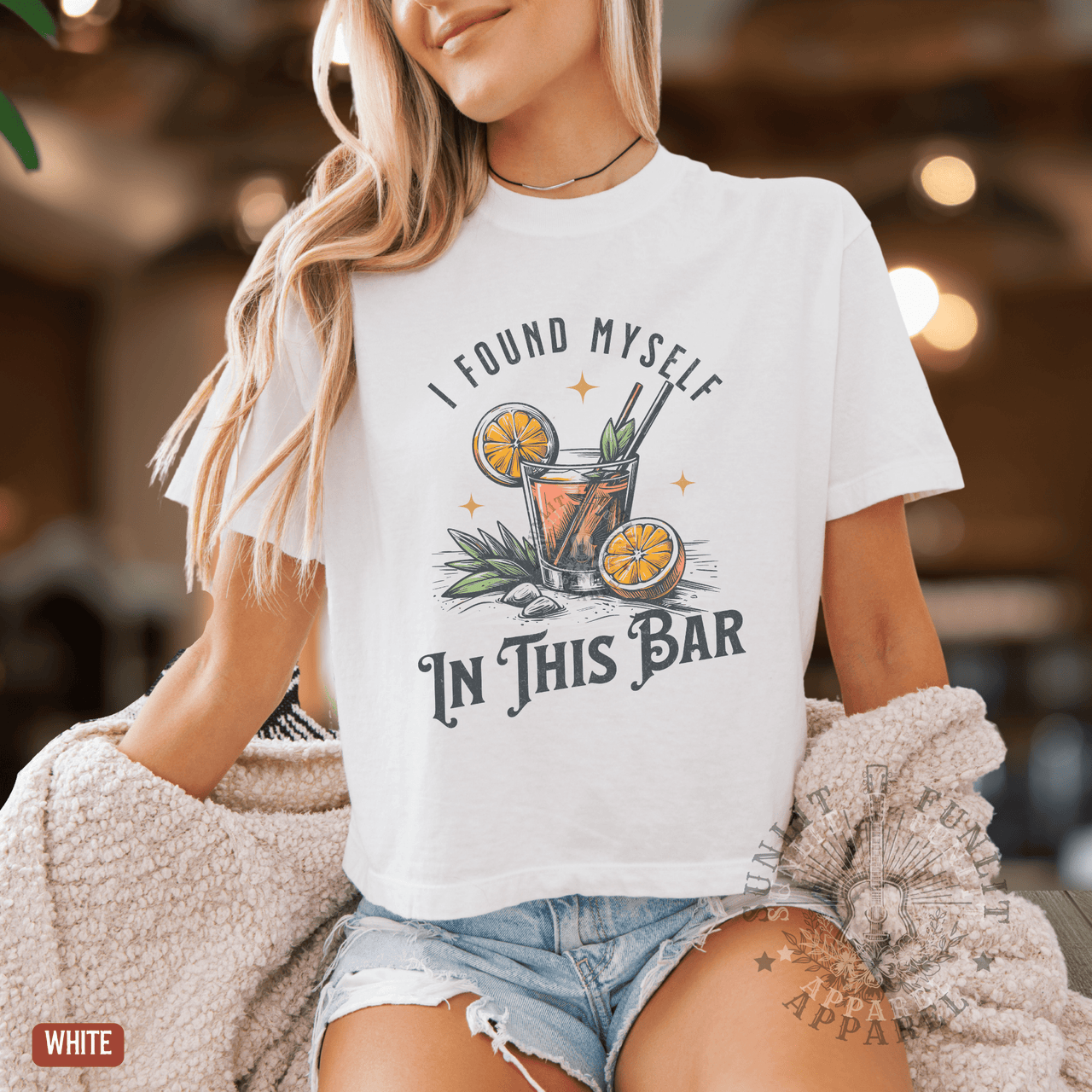 A woman wearing a white t-shirt with a graphic design of a cocktail and the text "I FOUND MYself IN THIS BAR" printed on it.