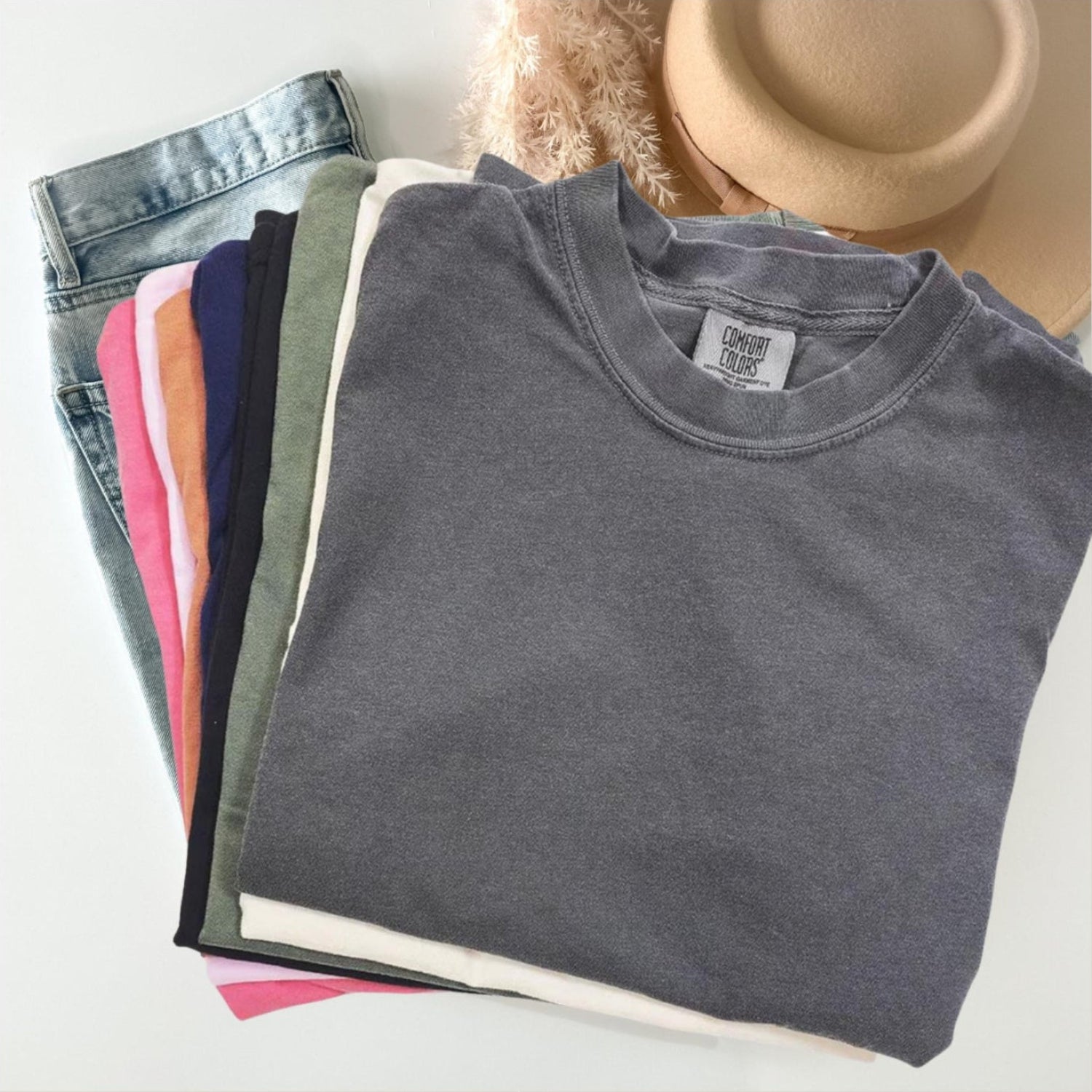 Stack of folded shirts with a hat on a white surface