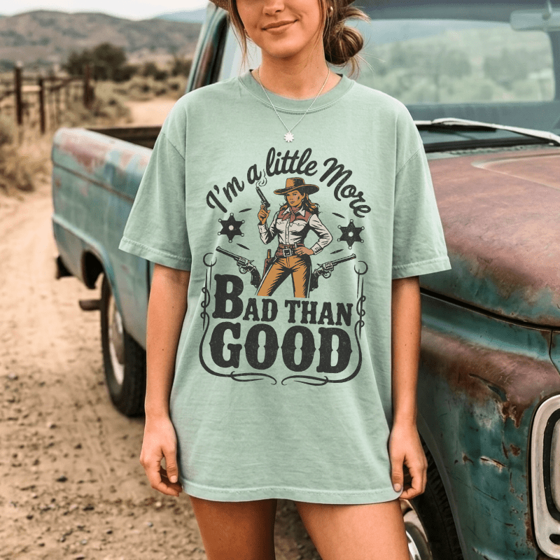 Person wearing a t-shirt with a graphic design and text, standing next to an old truck in a desert setting.