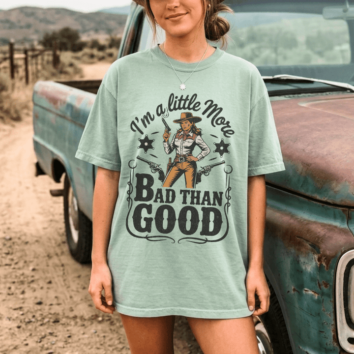 Person wearing a t-shirt with a graphic design and text, standing next to an old truck in a desert setting.