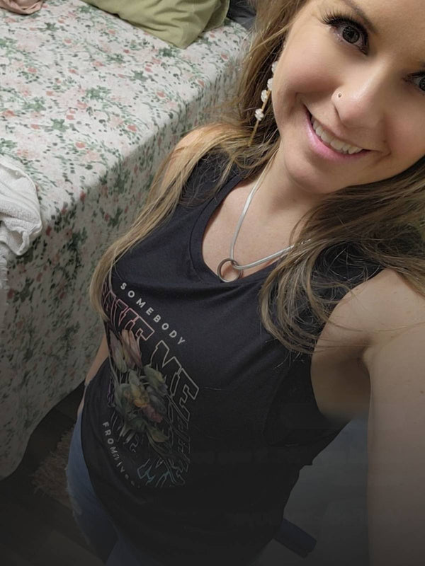 Woman wearing a black tank top with graphic design in a bedroom setting