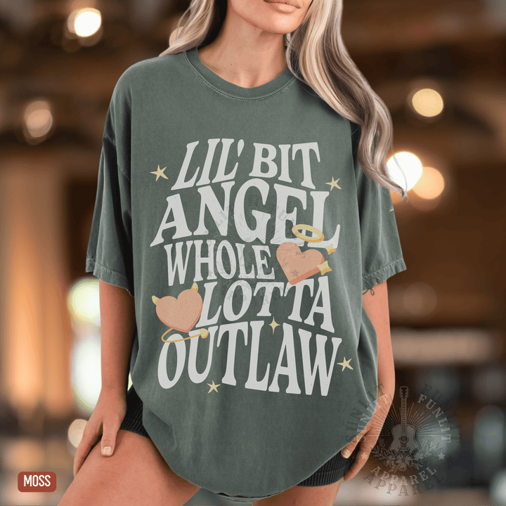 A woman wearing a green t-shirt with the text "Lil' Bit Angel Whole Lotta Outlaw" printed on it.