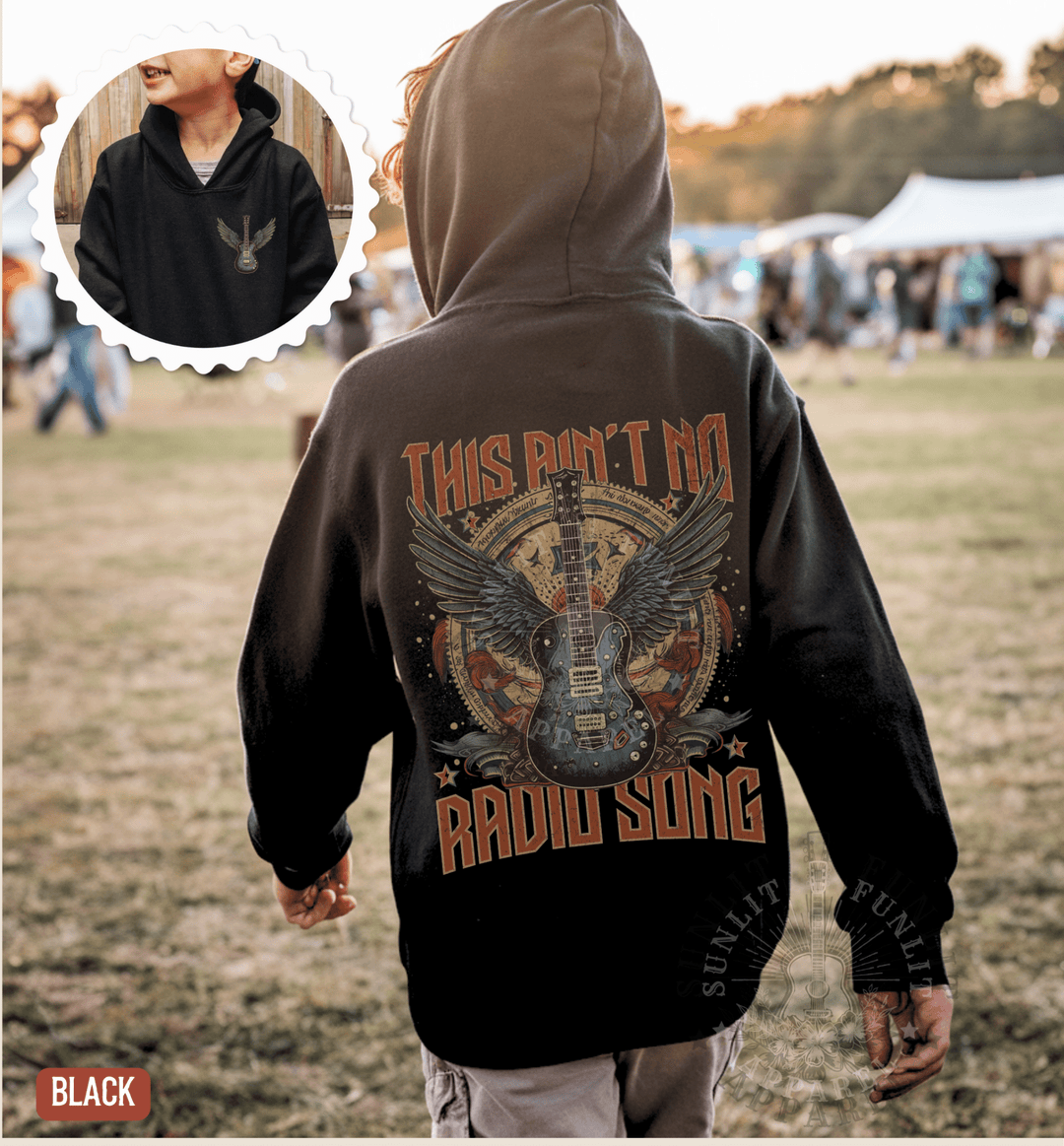 A person wearing a black hoodie with a graphic design of a guitar and the text "This Ain't No RADIO SONG" printed on it, standing in a grassy field.