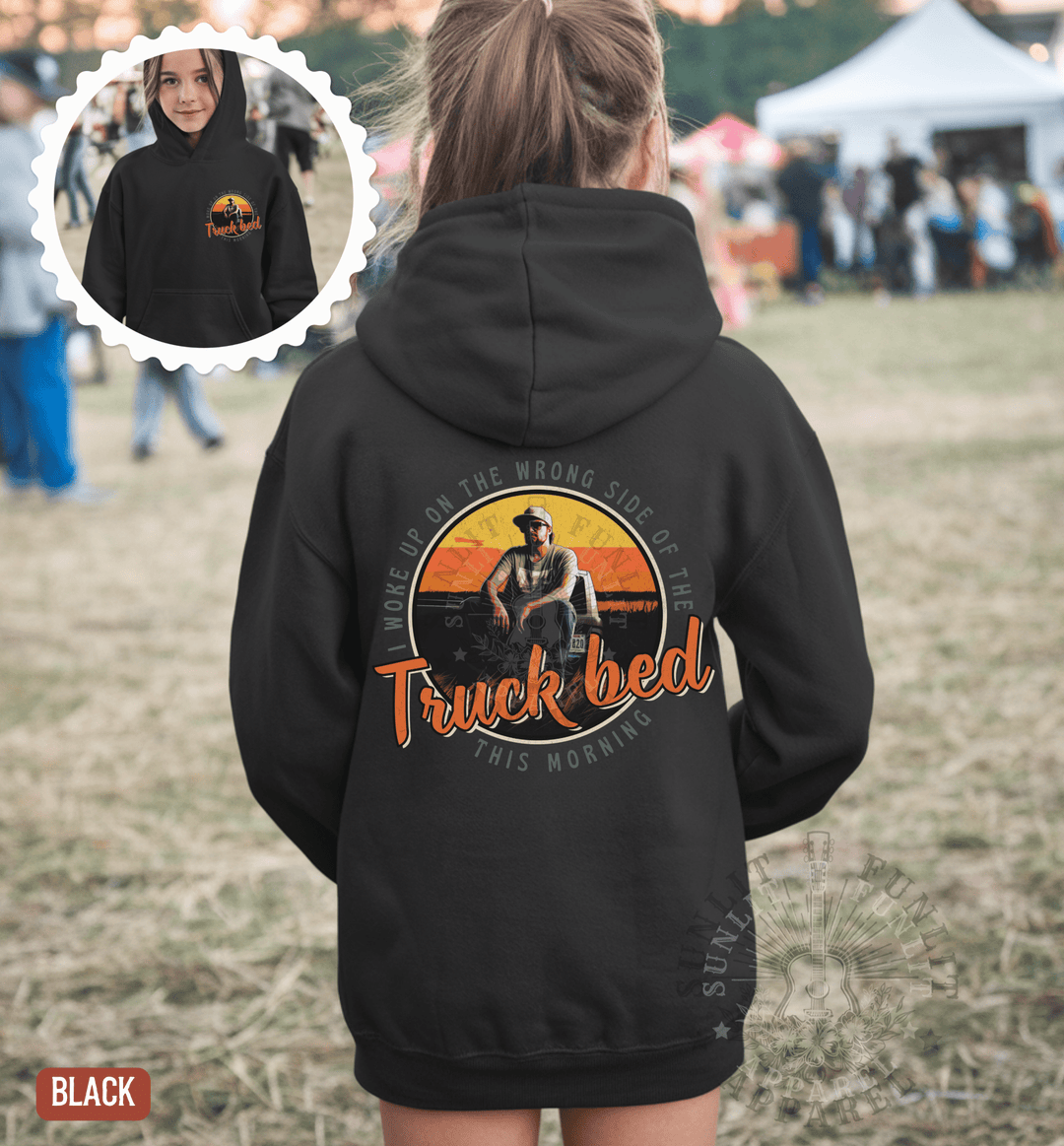 A person wearing a black hoodie with a graphic design on the back, including a cowboy hat and the text "Truck bed" and "Worship on the rough side of the road this morning".