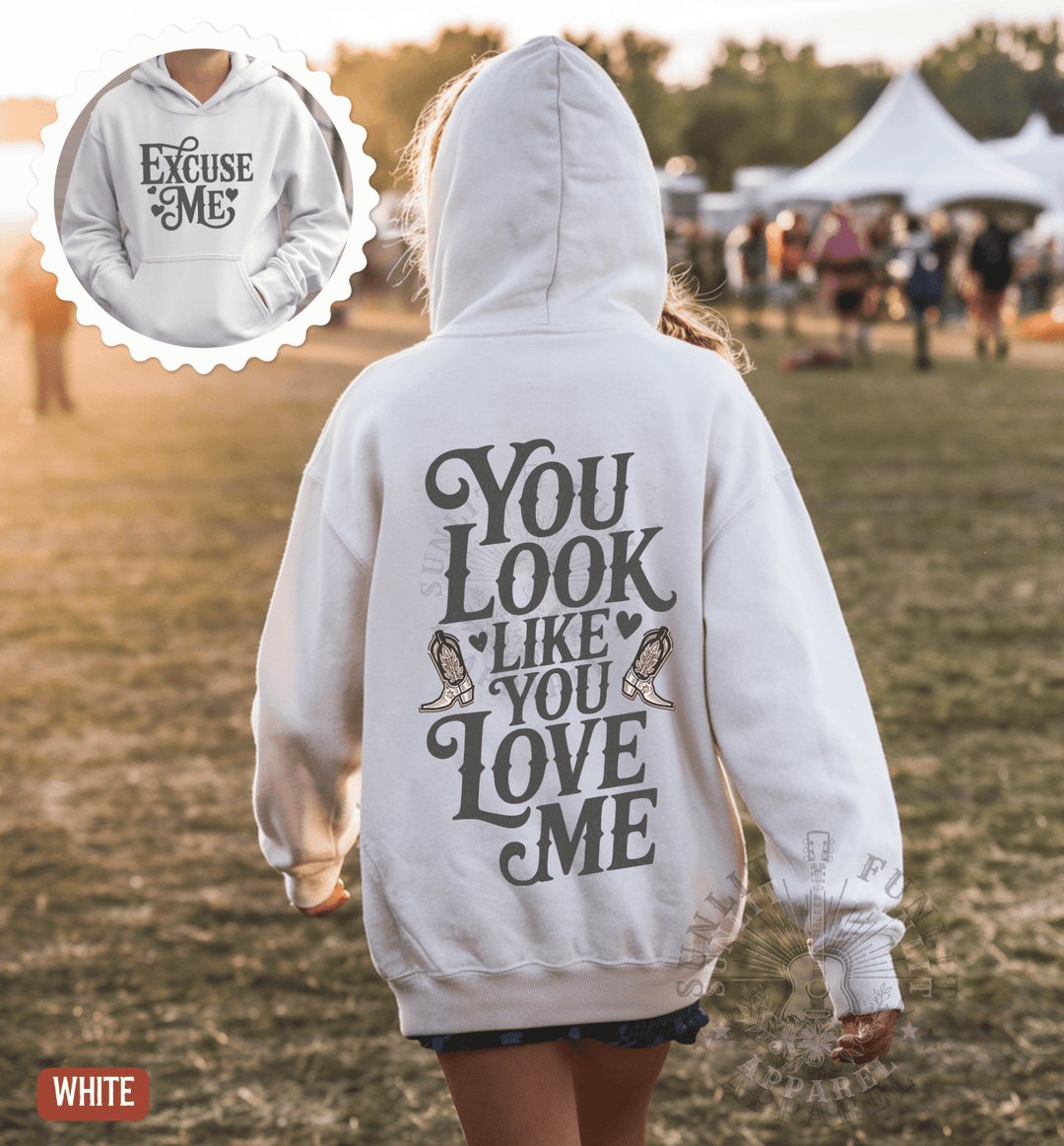 A person wearing a white hoodie with the text "You Look Like You Love Me" printed on it, walking in a field.