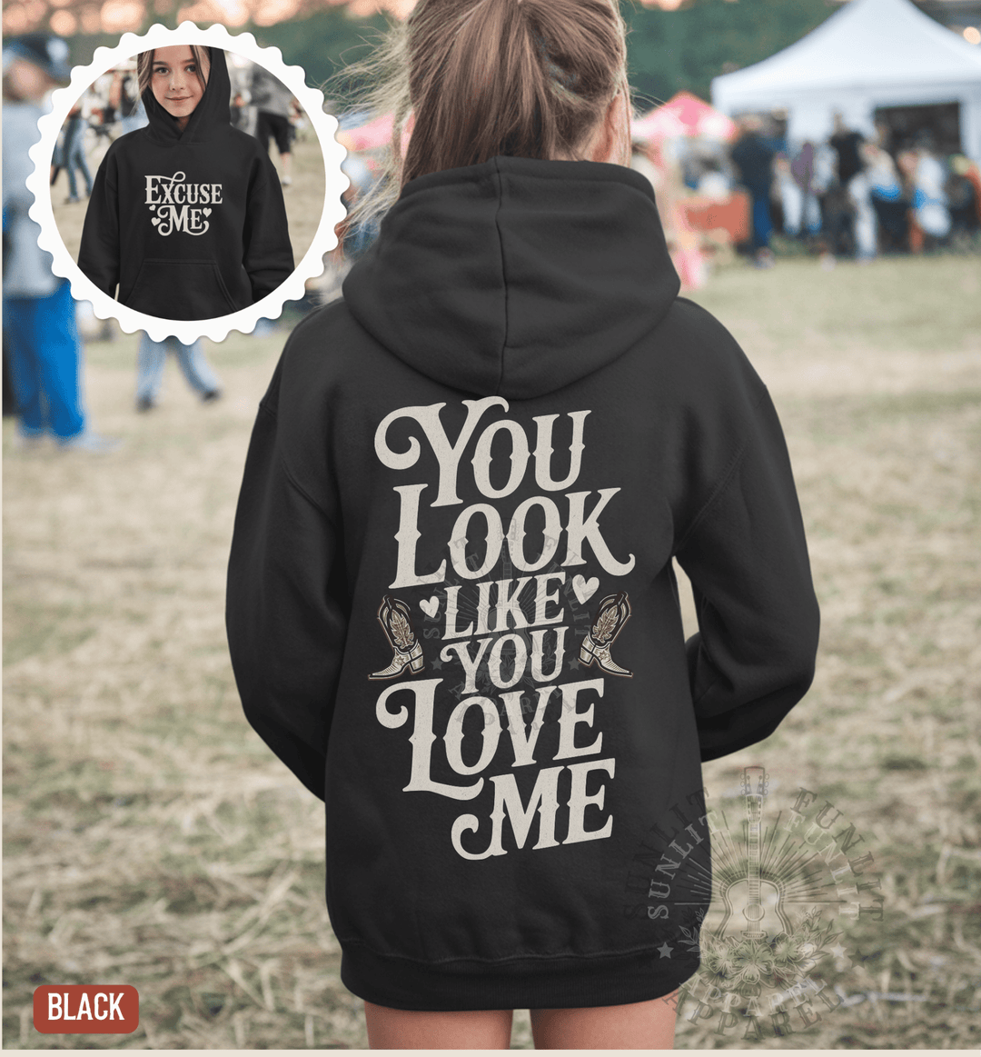 A person wearing a black hoodie with the text "YOU LOOK LIKE YOU LOVE ME" printed on the back.
