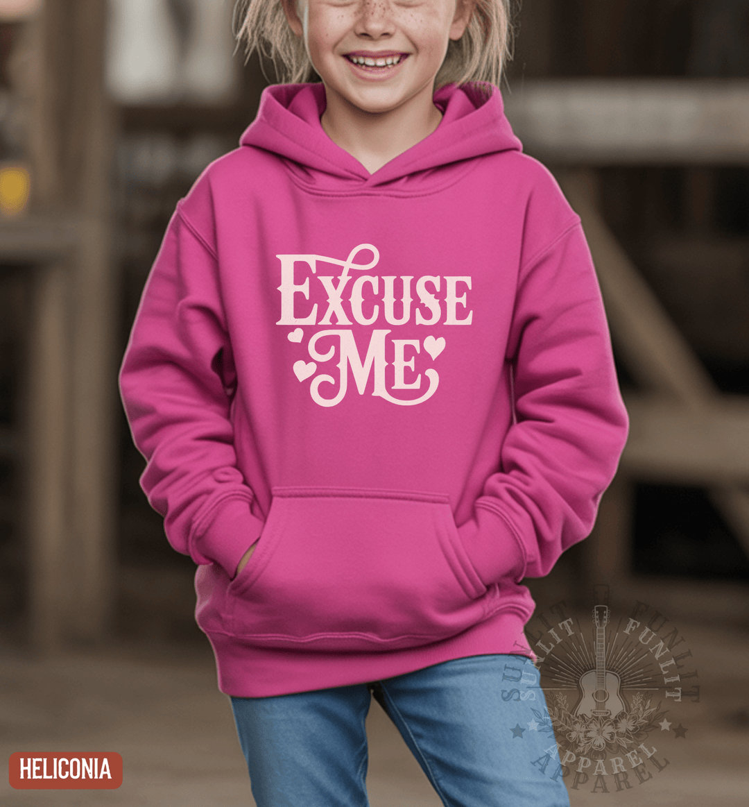A young girl wearing a pink hoodie with the text "Excise Me" printed on it, smiling and posing for the camera.